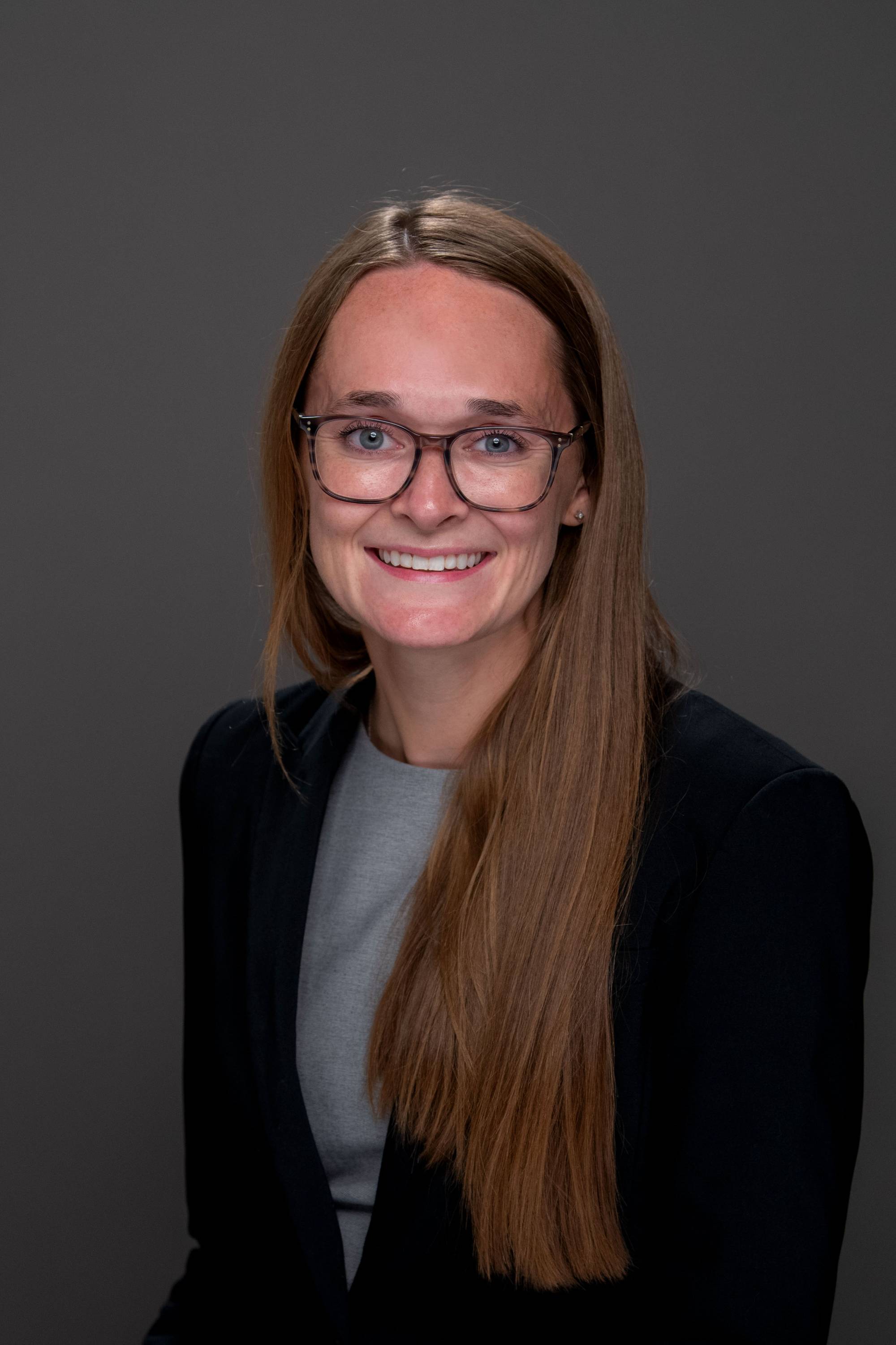 Emily Zeliasko portrait photo with a black blazer and gray shirt on with glasses.